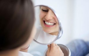 Женщина осматривет зубы в зеркале