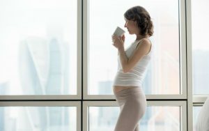 Беременная женщина пьёт чай у окна