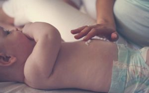 Мама наносит увлажняющий крем на живот ребёнка